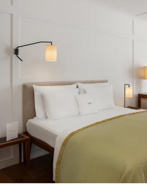 Comfortable hotel room with double bed, desk, armchairs and large windows with curtains at the LOUIS Hotel Munich.