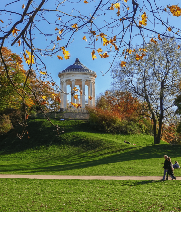 Tempel im Englischen Garten München, umgeben von herbstlichen Bäumen und grüner Wiese, blauer Himmel im Hintergrund.
