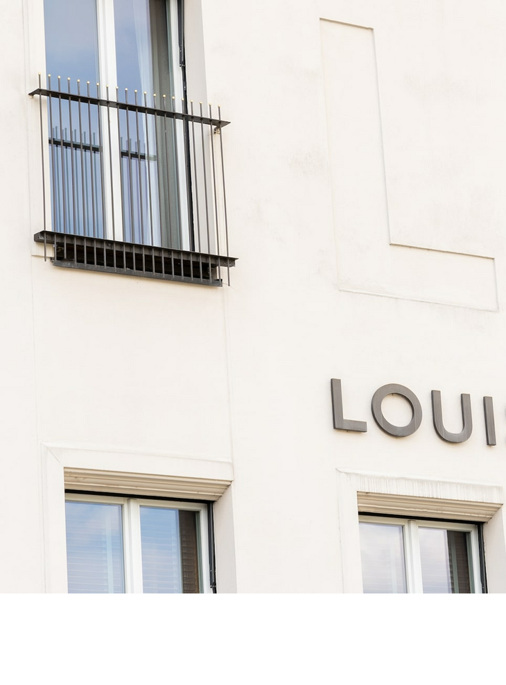 Fassade des LOUIS Hotels in München mit großen Fenstern und Balkongittern.