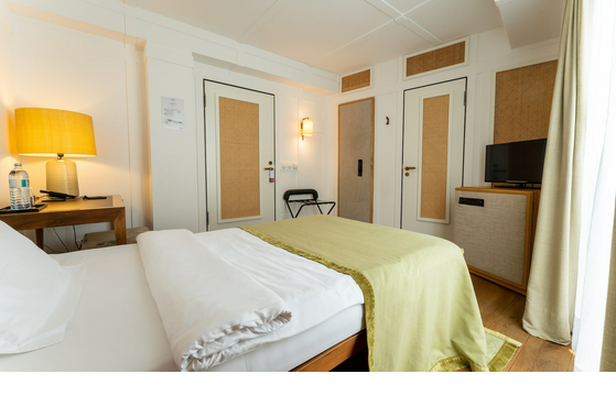 Bright hotel room with cozy bed, wooden details, desk, lamp and small TV.