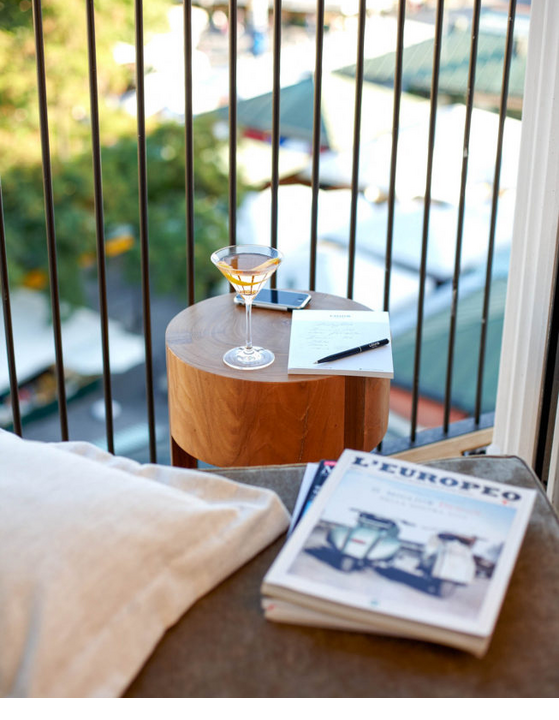 Blick vom Balkon des LOUIS Hotels: Tisch mit Drink, Notizblock, Stift und Buch, mit Aussicht auf grünen Markt.