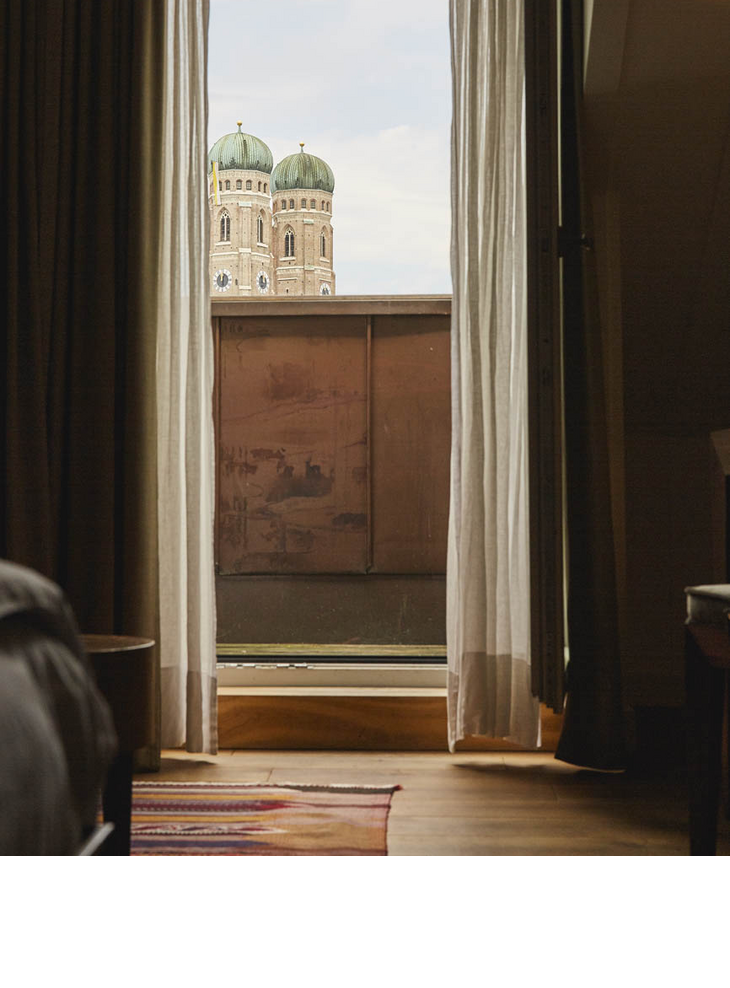 View from a hotel room of the towers of the Frauenkirche through a window with half-open curtains.