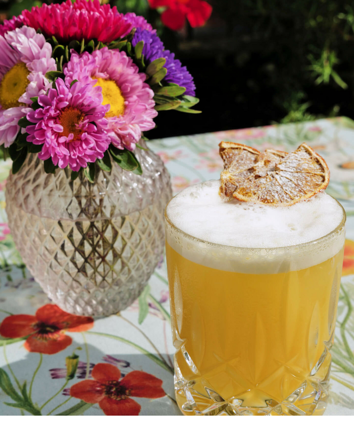 Blumenstrauß in Vase und Cocktail mit getrockneter Zitrone auf floralem Tisch.