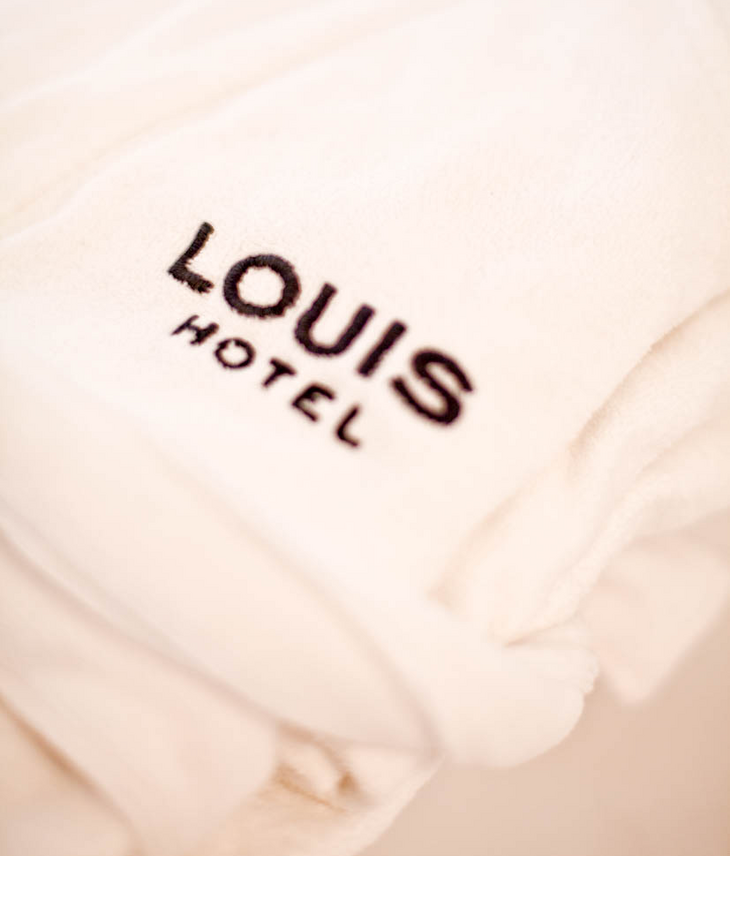 Weißer Hotelbademantel mit schwarzem LOUIS Hotel-Logo, weich und luxuriös.