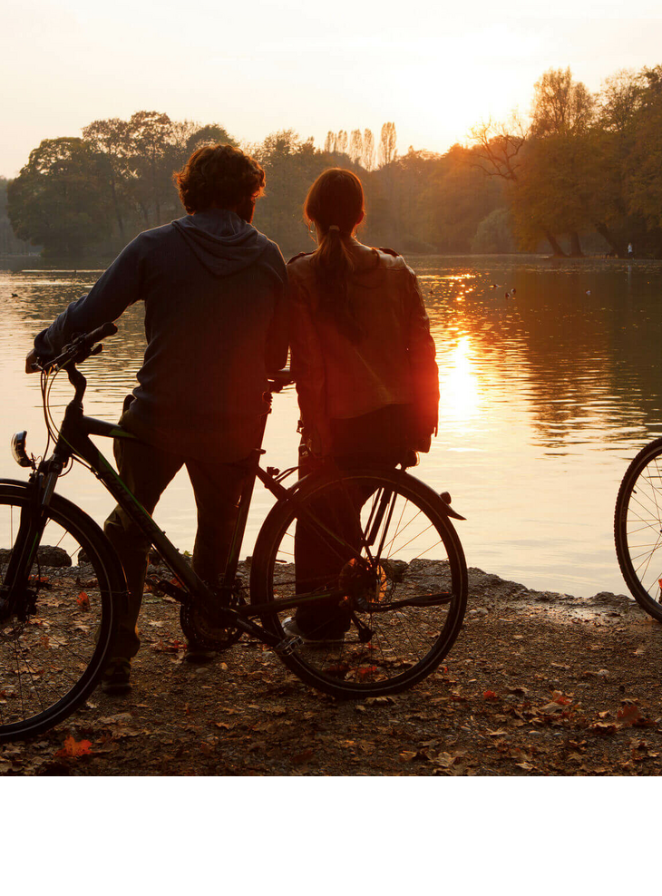 Radfahren zu jeder Jahreszeit Zwei Menschen mit Fahrrädern stehen am Seeufer und genießen den Sonnenuntergang.