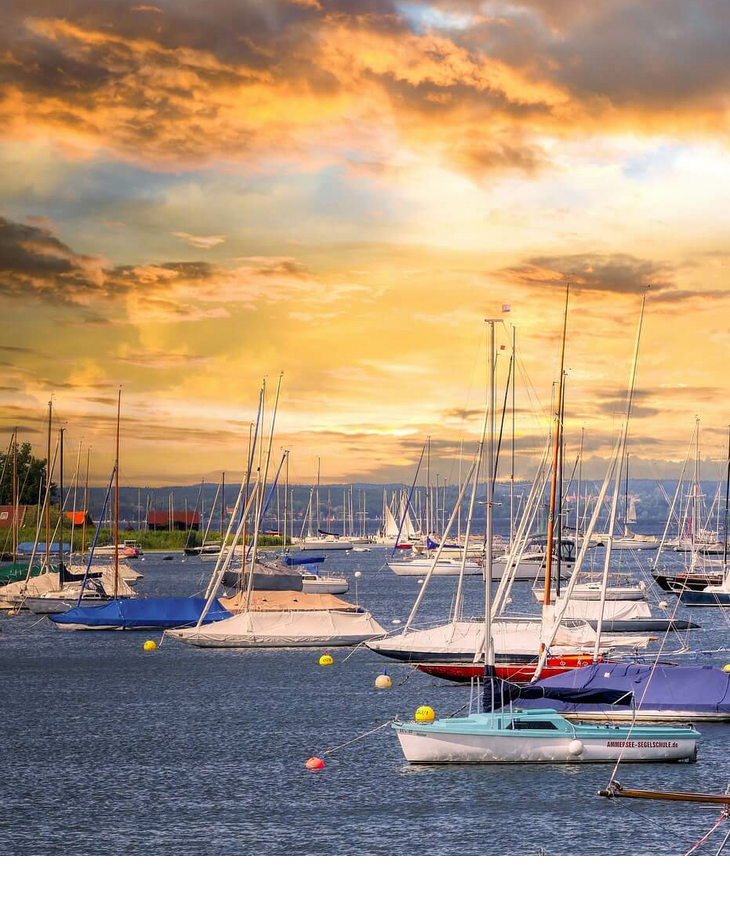 Sailboats in the harbor at sunset, surrounded by calm waters and a dramatic sky.