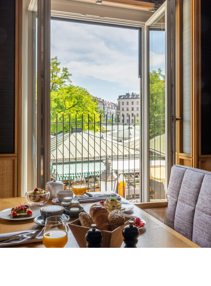 Breakfast LOUIS Hotel Munich Breakfast table in the LOUIS Hotel with a view of the Viktualienmarkt through an open window.