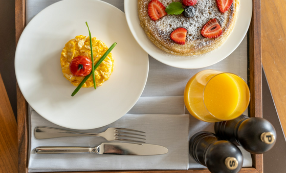 Breakfast in the hotel room LOUIS Hotel Munich Breakfast tray with scrambled eggs, tomato, pancakes with berries, orange juice and spice grinders at the LOUIS Hotel Munich.