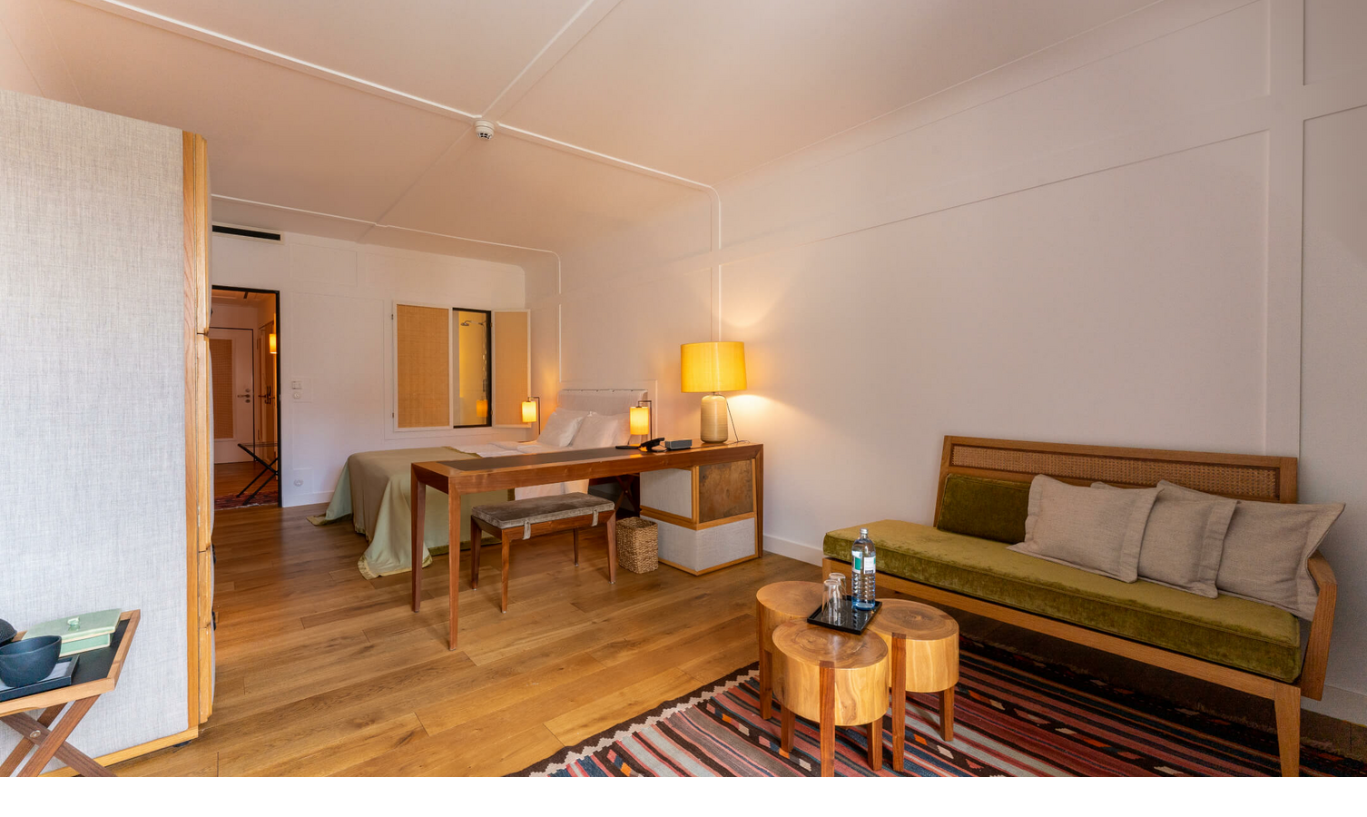 Helles Hotelzimmer mit Holzboden, Bett, Schreibtisch, Sofa, Teppich und Tischlampen im LOUIS Hotel München.
