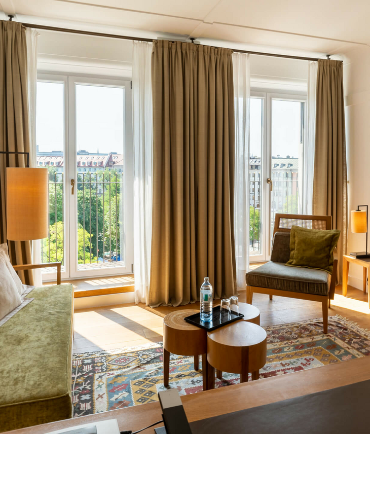 LOUIS Hotel München | Zimmer Market View Deluxe Helles Hotelzimmer mit modernen Möbeln, großen Fenstern und Blick auf die Stadt im LOUIS Hotel München.
