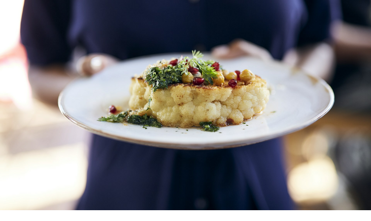Cauliflower steak at the restaurant A plate of artfully arranged cauliflower, garnished with herbs and pomegranate seeds.