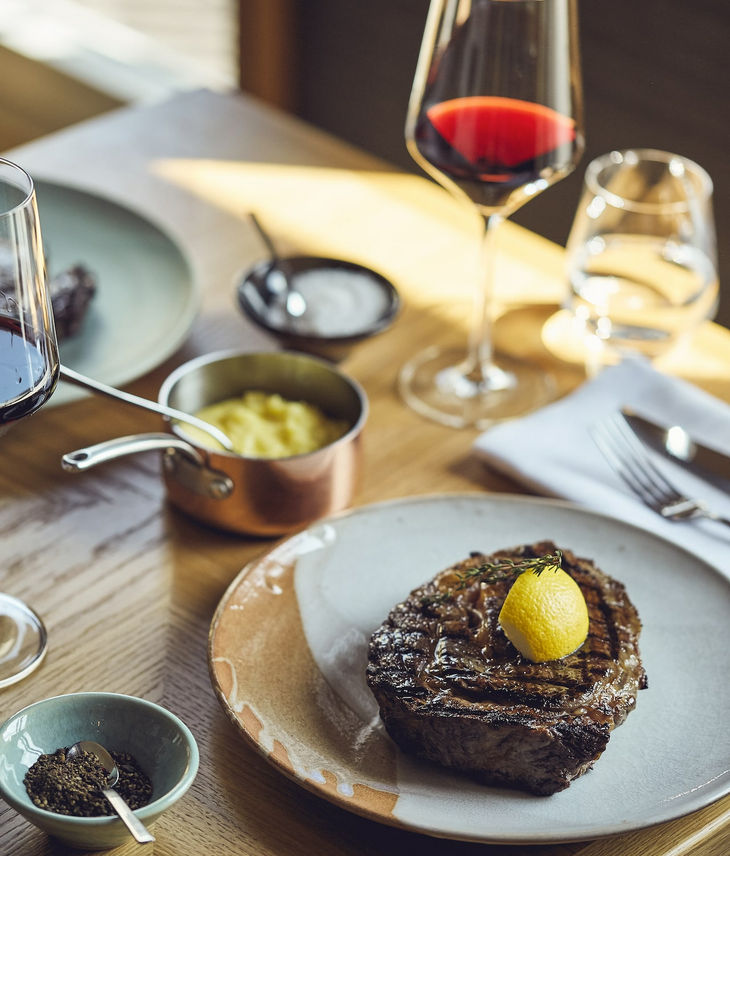 Steak mit Zitrone, Rotweinglas, Kartoffelpüree und Gewürzen auf Holztisch im LOUIS Hotel München.