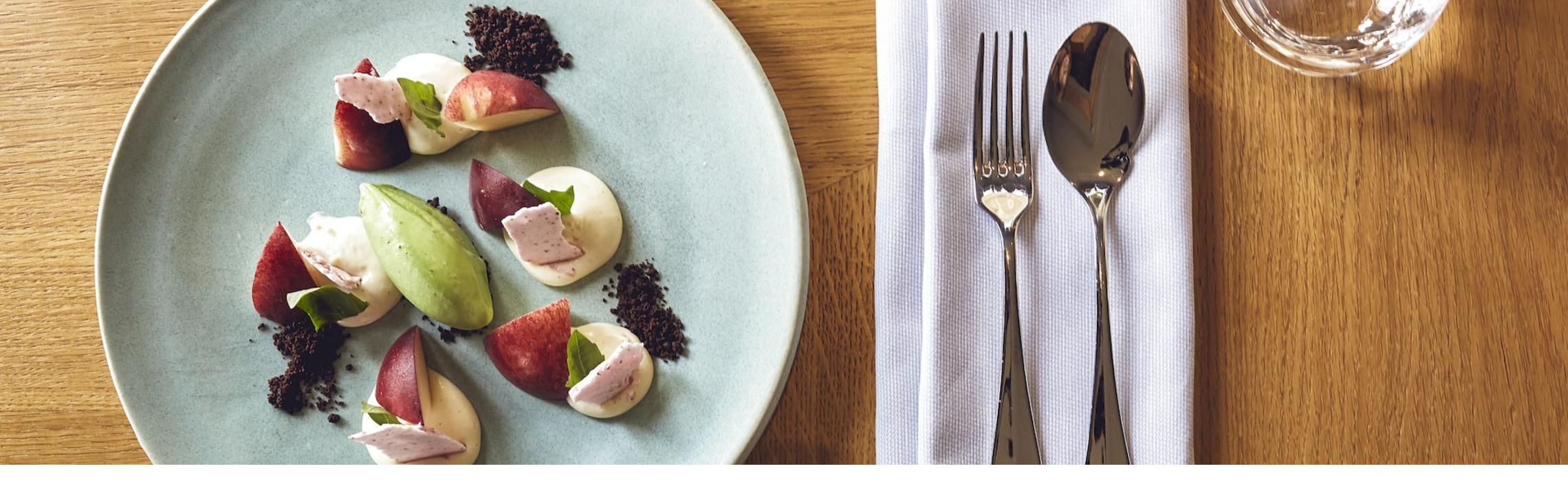 Grillroom Restaurant ice cream dessert LOUIS Hotel Munich Elegant dessert on a blue plate with cutlery and glasses on a wooden table in the LOUIS Hotel Munich.
