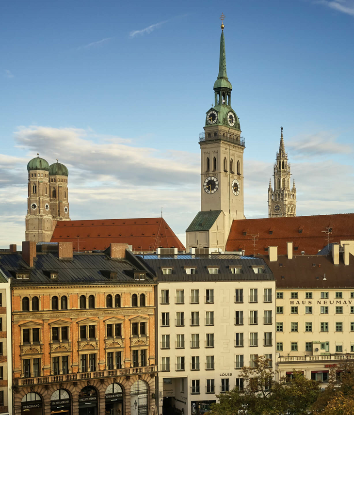The LOUIS Hotel in München | Angebot "Fall in love with Munich" Blick auf Münchens Altstadt mit historischen Türmen und Gebäuden bei klarem Himmel.